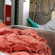 Masked worker standing in front of large container of raw ground beef